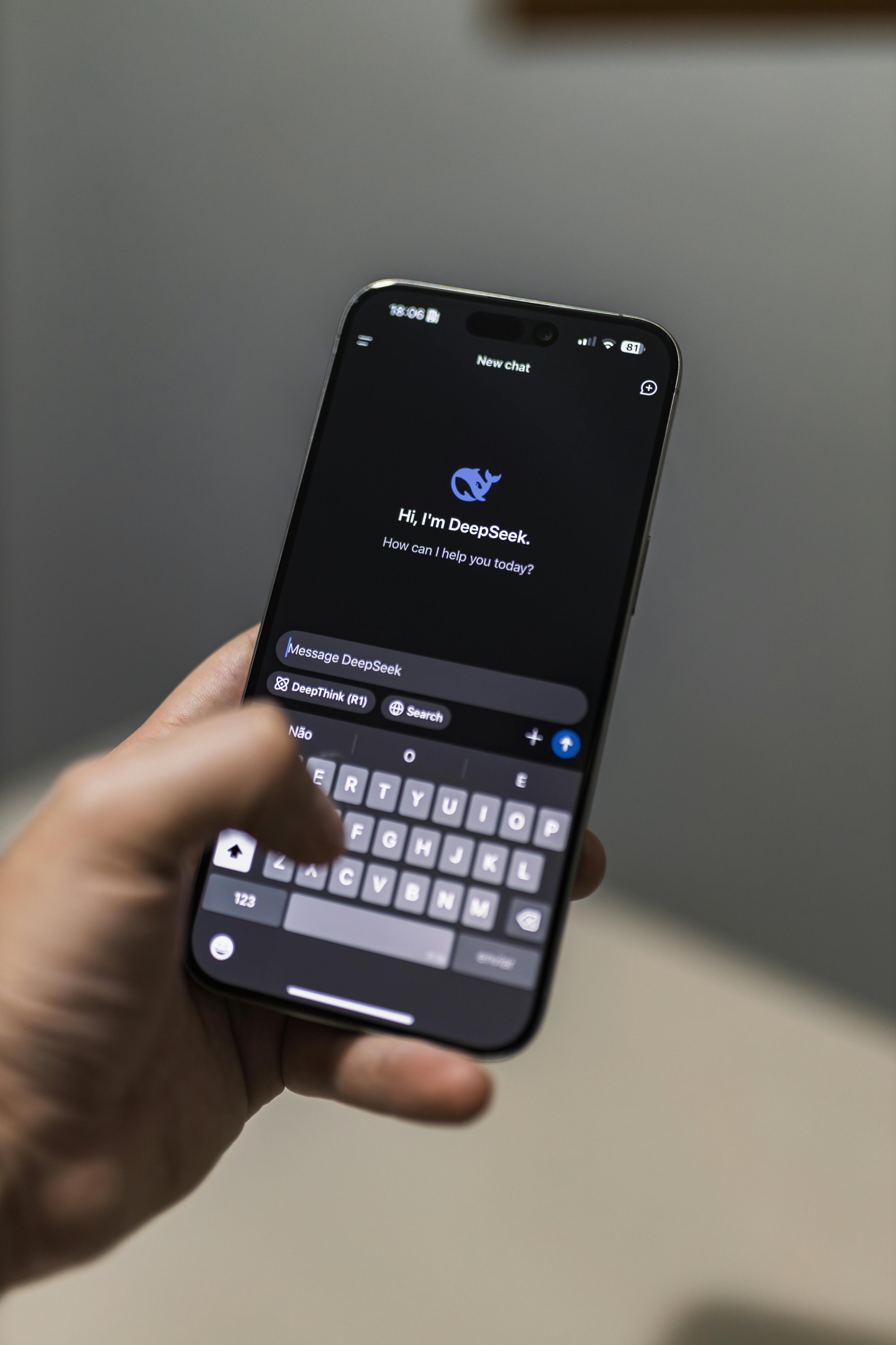 Nahaufnahme einer Person, die ein Smartphone hält, auf dem ein Chat-Interface mit der Begrüßung "Hi, I'm DeepSeek. How can I help you today?" zu sehen ist. Die Person tippt auf einer virtuellen Tastatur.